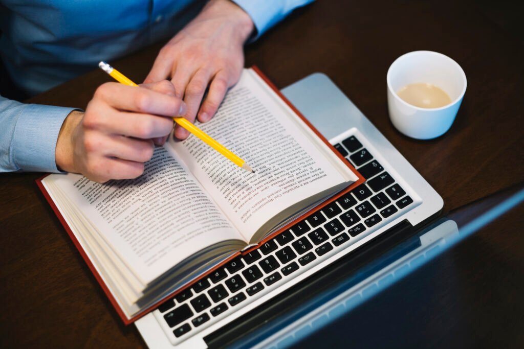 A person editing a book with a pencil, laptop, and a cup of coffee, perfect for book proofreading.